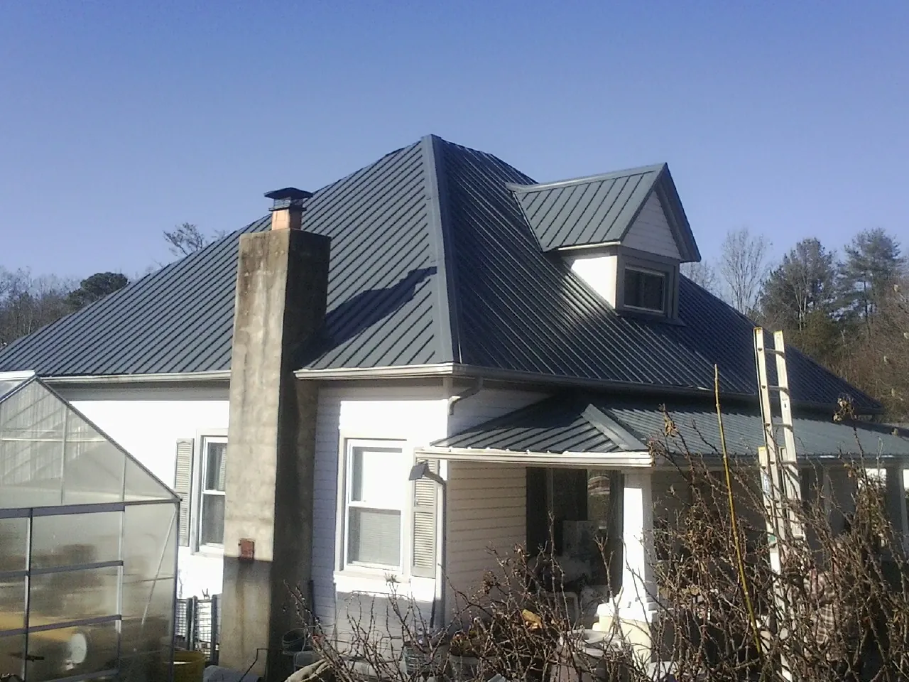 Dark blue standing seam metal roof on a white farmhouse with dormer — Slate & Tile Roof Repair by Roofing Brothers in Lake Lillian