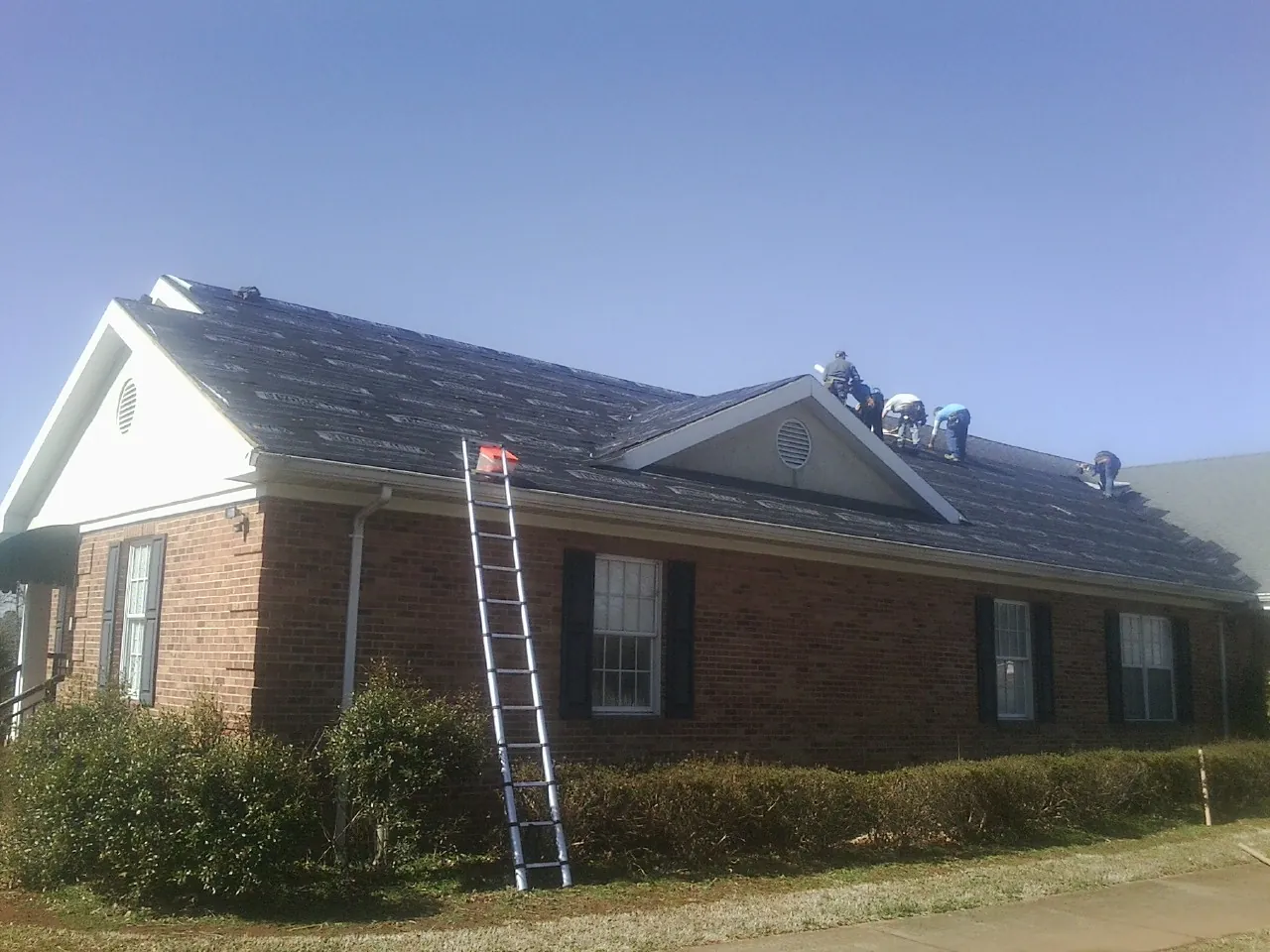 Crew tearing shingles off a brick ranch roof with a ladder set — Metal Roof Repair work by our crew in Lake Lillian