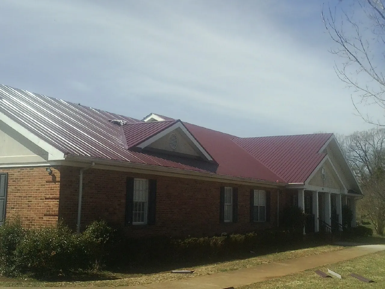 Red metal roof with gabled entries on a long brick building, from a Hail Damage Roof Repair job in Lake Lillian