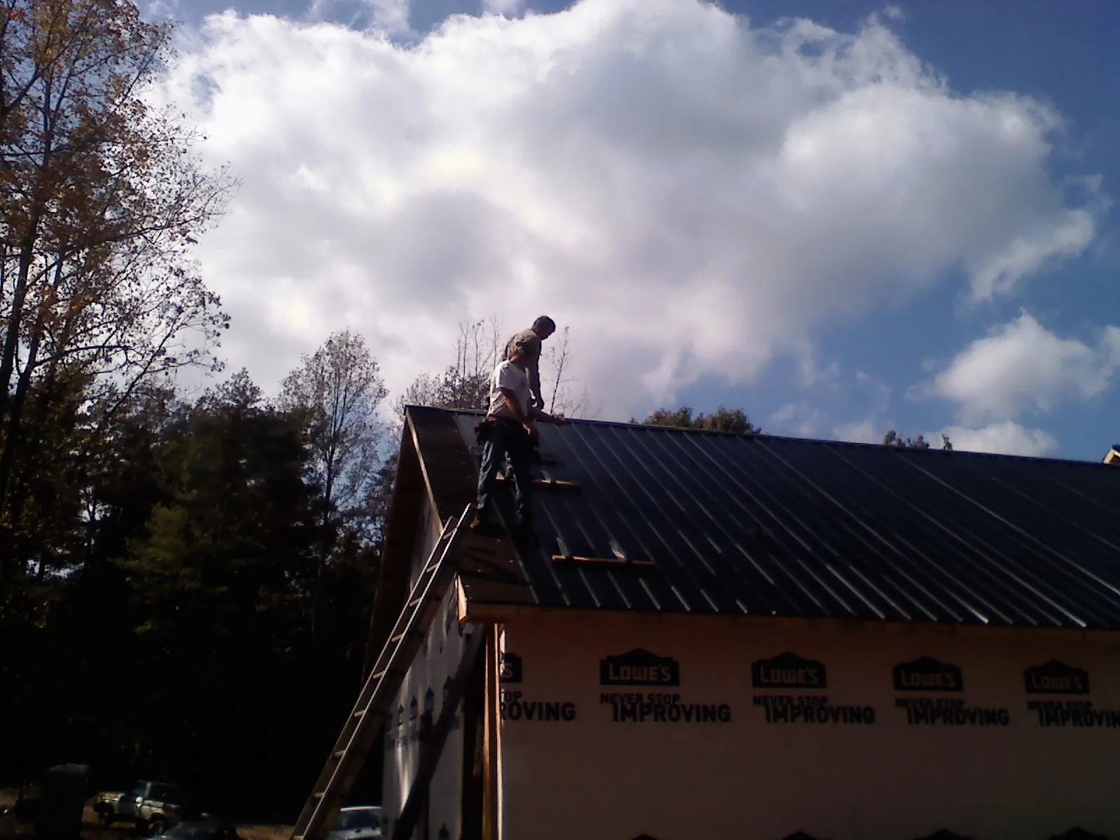 Roofer fastening dark metal panels high against a cloudy sky, from a Roof Inspection job in Lake Lillian
