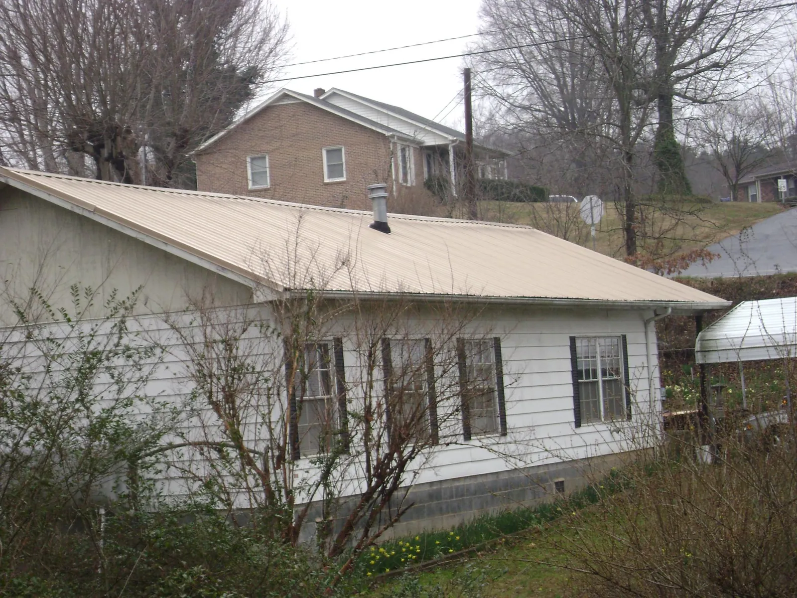 Tan metal roof on a white sided house set into a hillside — Commercial Roofing by Roofing Brothers in Lake Lillian